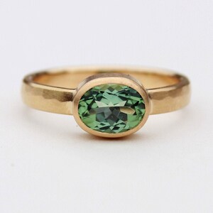 May include: A gold ring with a hammered band and a green oval gemstone.
