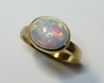 May include: A gold ring with a white opal gemstone set in a bezel setting. The opal has a rainbow of colors.