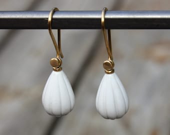 Puede incluir: Un par de pendientes de cerámica blanca en forma de lágrima con detalles dorados que cuelgan de una barra de metal.