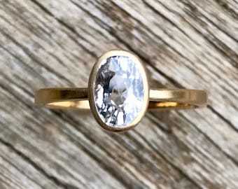 May include: A gold ring with a clear oval-shaped gemstone set in a bezel setting.