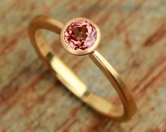 May include: A delicate gold ring with a single round pink gemstone set in a bezel setting.