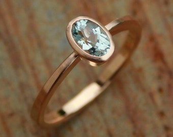May include: A delicate rose gold ring with a light blue oval-shaped gemstone.