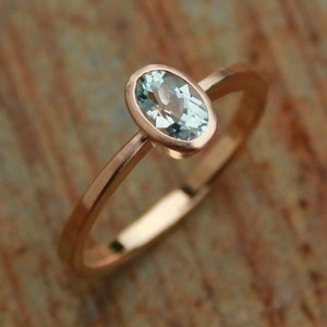May include: A delicate rose gold ring with a light blue oval-shaped gemstone.