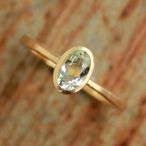 May include: A gold ring with a light green oval gemstone set in a bezel setting.