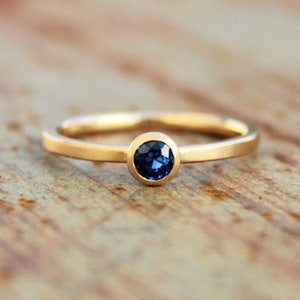 May include: A simple gold band ring with a bezel-set blue sapphire gemstone.
