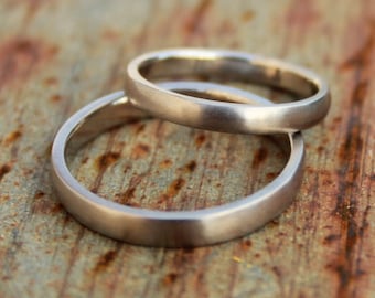 May include: Two silver wedding bands stacked on top of each other on a rusty metal surface.