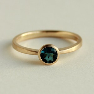 May include: A gold ring with a round, dark blue gemstone.