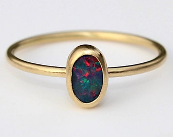 May include: A gold ring with a dark green, red, and black oval opal gemstone.