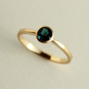 May include: A gold ring with a round, dark blue gemstone set in a bezel setting.