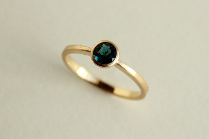 May include: A gold ring with a round, dark blue gemstone set in a bezel setting.