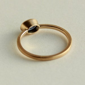May include: A simple gold band ring with a small, round, blue gemstone set in a bezel setting.