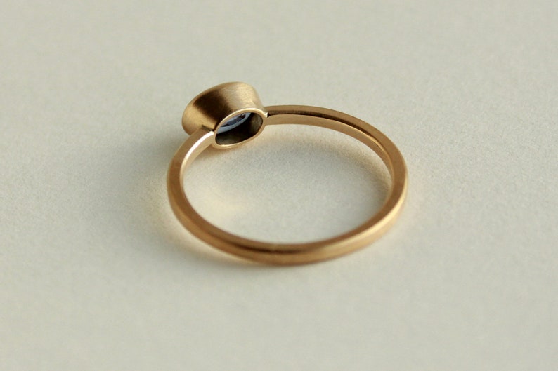 May include: A simple gold band ring with a small, round, blue gemstone set in a bezel setting.