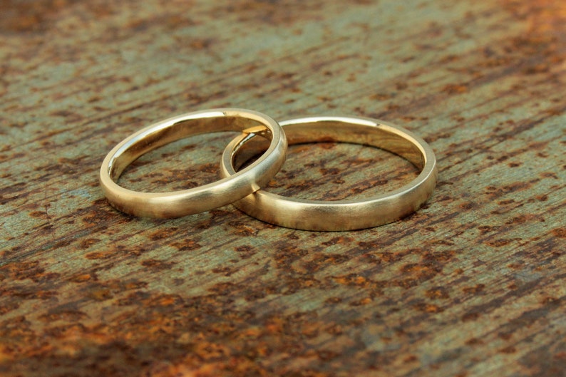 以下が含まれることがあります： さびた金属製の表面に置かれた2つの金の結婚指輪