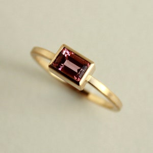 May include: A gold ring with a pink rectangular gemstone set in a gold bezel.