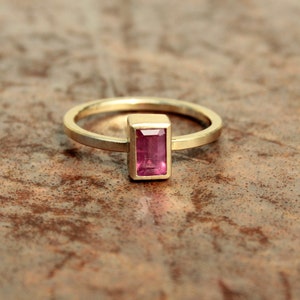 May include: A gold ring with a rectangular pink gemstone set in a gold bezel.