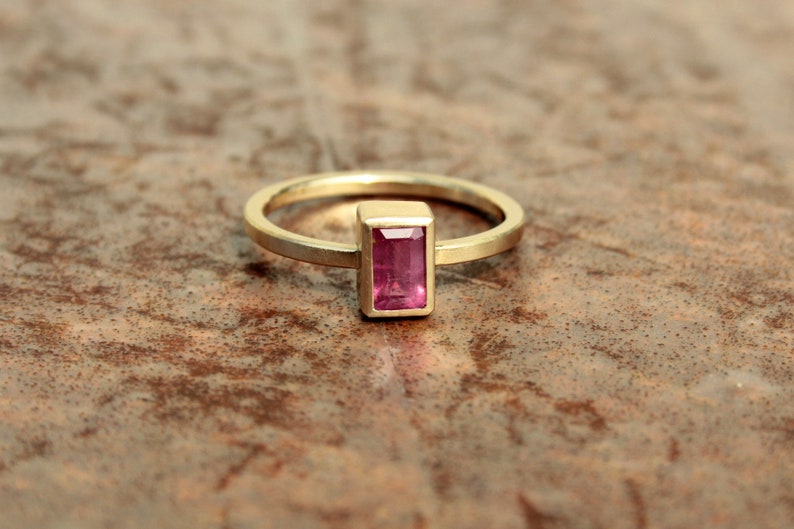 May include: A gold ring with a rectangular pink gemstone set in a gold bezel.