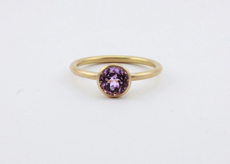 May include: A gold ring with a bezel set purple gemstone.