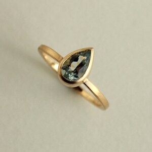 May include: A delicate gold ring with a pear-shaped aquamarine gemstone set in a bezel setting.