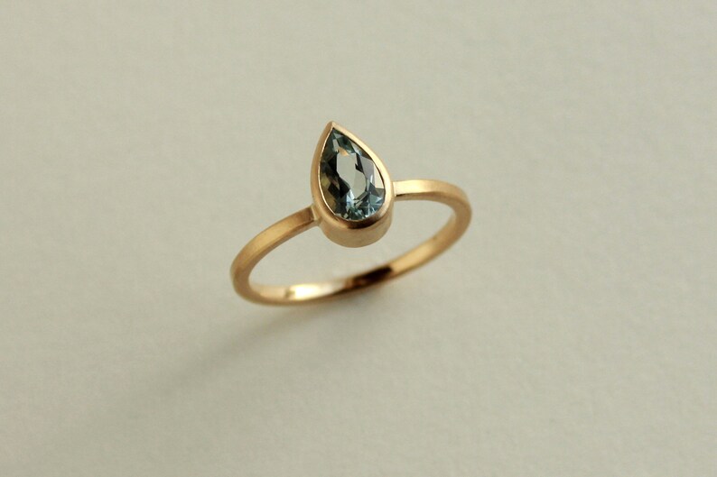 May include: A gold ring with a teardrop-shaped blue gemstone.