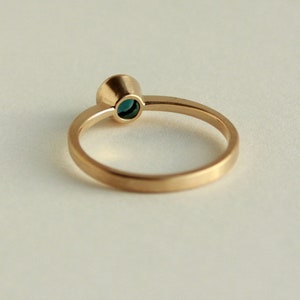 May include: A gold ring with a small, round, teal-colored gemstone set in a bezel setting.