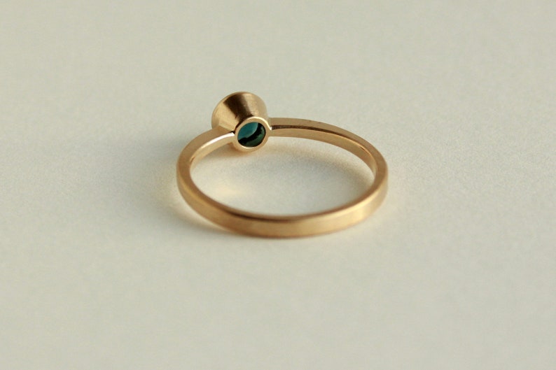 May include: A gold ring with a small, round, teal-colored gemstone set in a bezel setting.