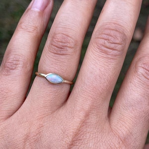May include: A delicate gold ring with a marquise-shaped opal gemstone. The opal is a milky white color with a slight iridescent shimmer.