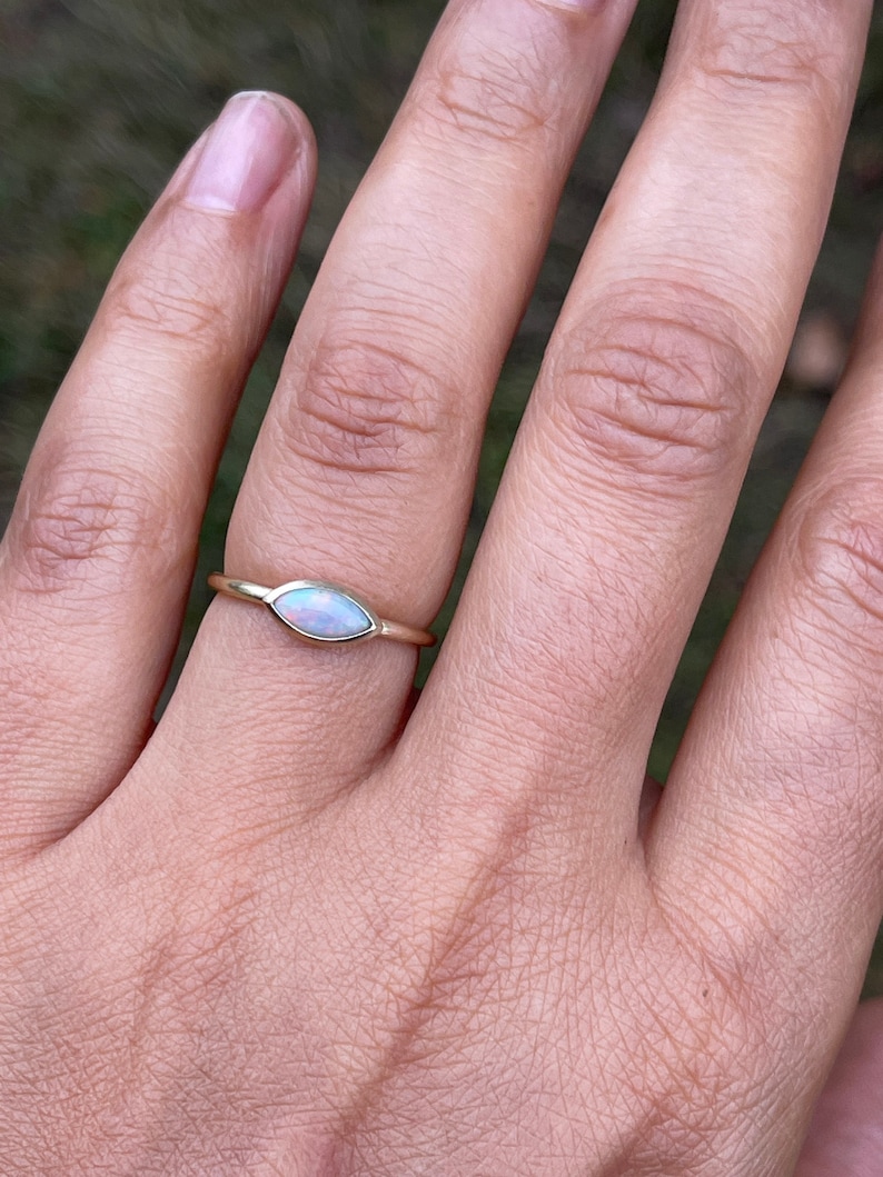 May include: A delicate gold ring with a marquise-shaped opal gemstone. The opal is a milky white color with a slight iridescent shimmer.