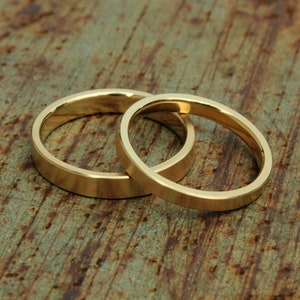 May include: Two gold wedding bands, one slightly larger than the other, are intertwined and resting on a rustic wooden surface.