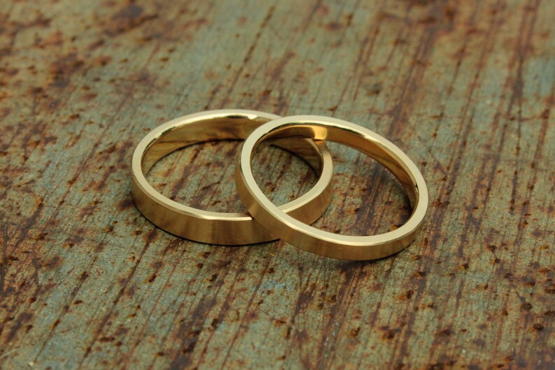 May include: Two gold wedding bands, one slightly larger than the other, are intertwined and resting on a rustic wooden surface.