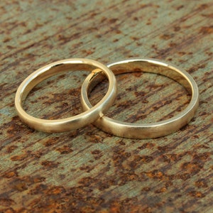 以下が含まれることがあります： さびた金属の表面に絡み合った2つの金の結婚指輪