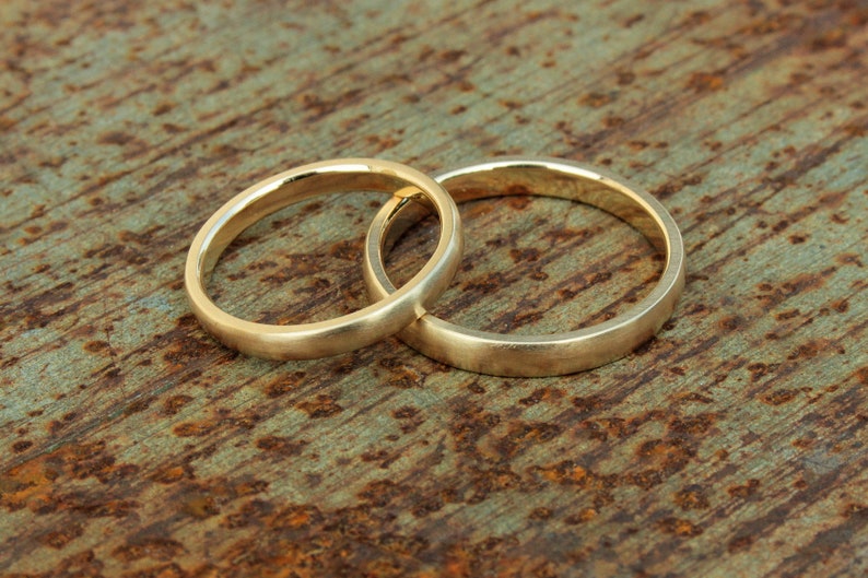 以下が含まれることがあります： さびた金属の表面に絡み合った2つの金の結婚指輪
