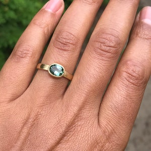 May include: A gold ring with a green oval gemstone. The ring is on a person's finger.