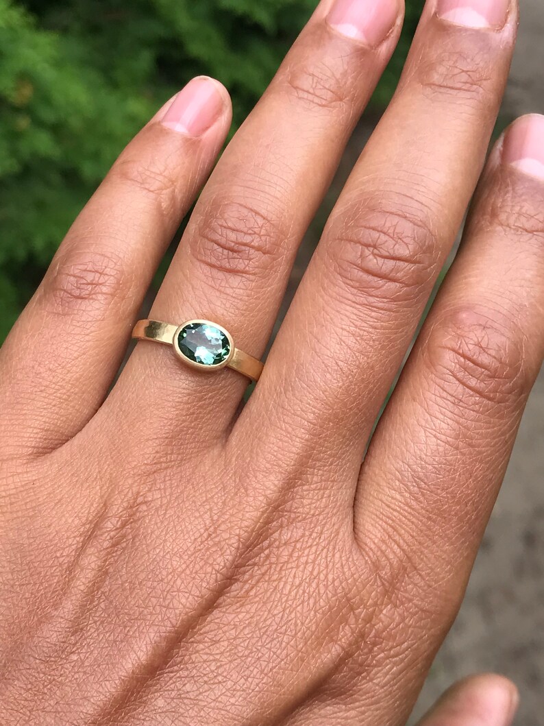 May include: A gold ring with a green oval gemstone. The ring is on a person's finger.