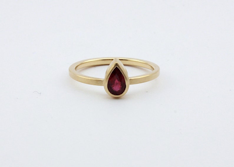 May include: A gold ring with a pear-shaped ruby gemstone.