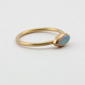 May include: A delicate gold band ring with a single, oval-shaped opal gemstone set in the center.