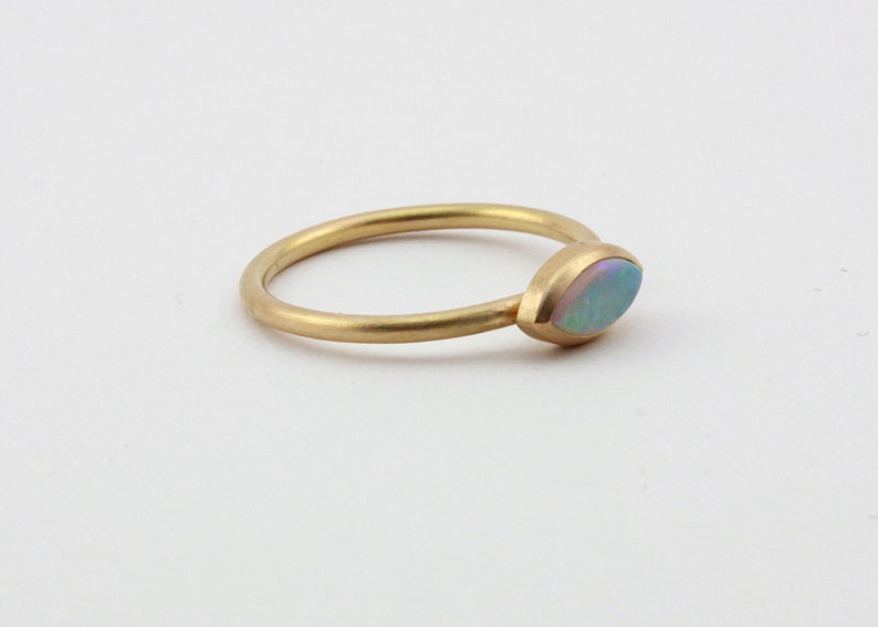 May include: A delicate gold band ring with a single, oval-shaped opal gemstone set in the center.