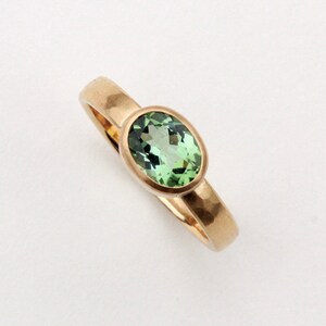 May include: A gold ring with a green oval gemstone set in a bezel setting. The band of the ring is hammered.