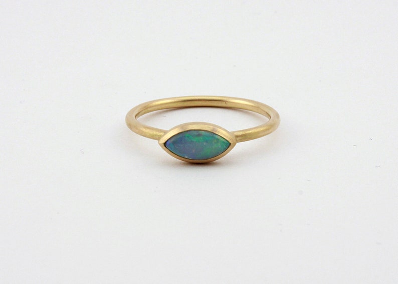 May include: A gold ring with a marquise-shaped opal gemstone. The opal is a light blue-green color with flashes of iridescent color.