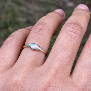 May include: A gold ring with a pear-shaped opal gemstone. The opal has a light blue and pink iridescent sheen.
