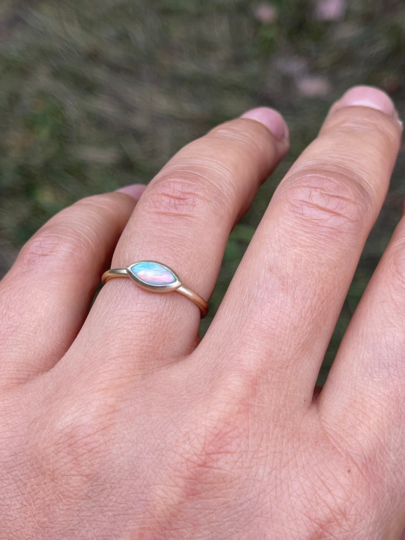 May include: A gold ring with a pear-shaped opal gemstone. The opal has a light blue and pink iridescent sheen.