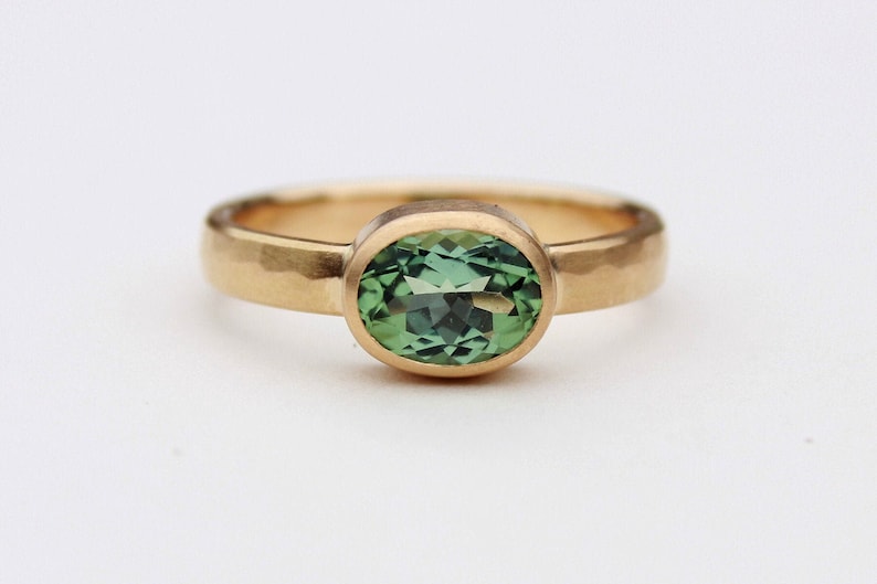 May include: A gold ring with a hammered band and a green oval gemstone.
