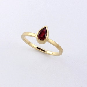 May include: A gold ring with a teardrop-shaped red gemstone.