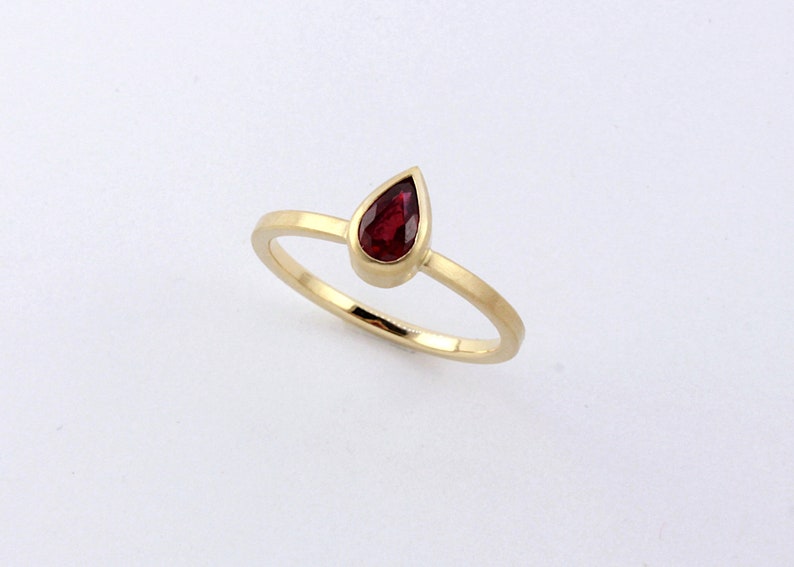 May include: A gold ring with a teardrop-shaped red gemstone.