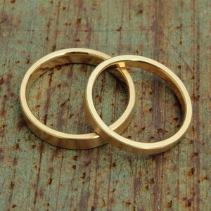 May include: Two gold wedding bands, interlocked, on a rustic, textured background.