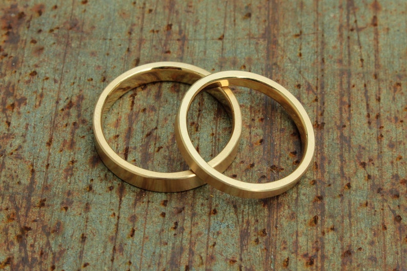 May include: Two gold wedding bands, interlocked, on a rustic, textured background.