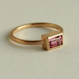 May include: A gold ring with a pink rectangular gemstone set in a gold bezel.