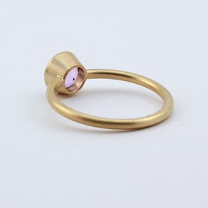 May include: A gold ring with a small, round, light purple gemstone set in the center.