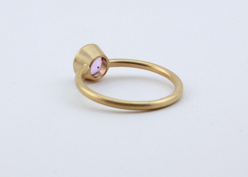 May include: A gold ring with a small, round, light purple gemstone set in the center.