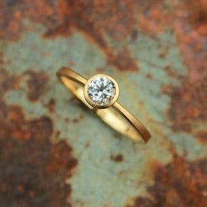 May include: A simple gold band ring with a bezel setting featuring a round, clear diamond.