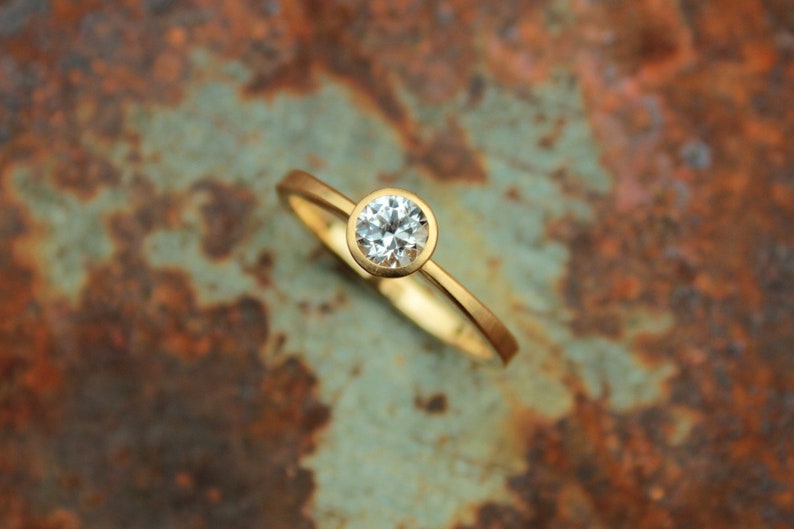 May include: A simple gold band ring with a bezel setting featuring a round, clear diamond.